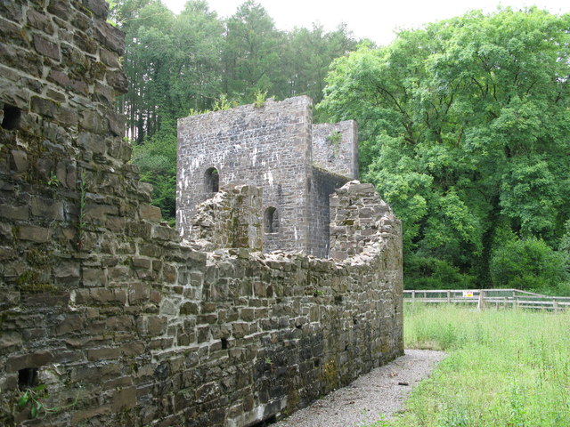 Roofless stone walls and a tall ruined engine house of Grove Colliery beside a gravel path and woodland.