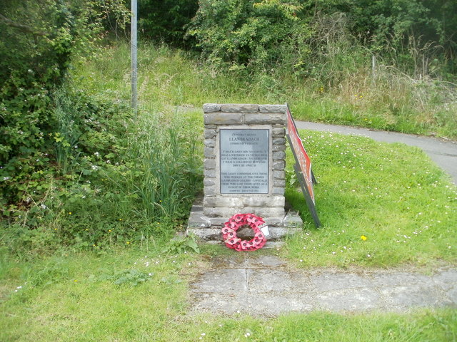 A rough stone memorial cairn with an inscribed plaque, standing on grass near the former colliery site.