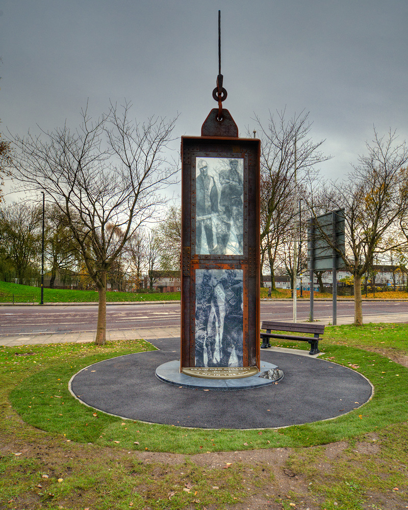 An eight-metre steel memorial shaped like a mine lift cage, with glass panels showing miners, standing on the site of the former Bradford Colliery near the Etihad Campus, Manchester.