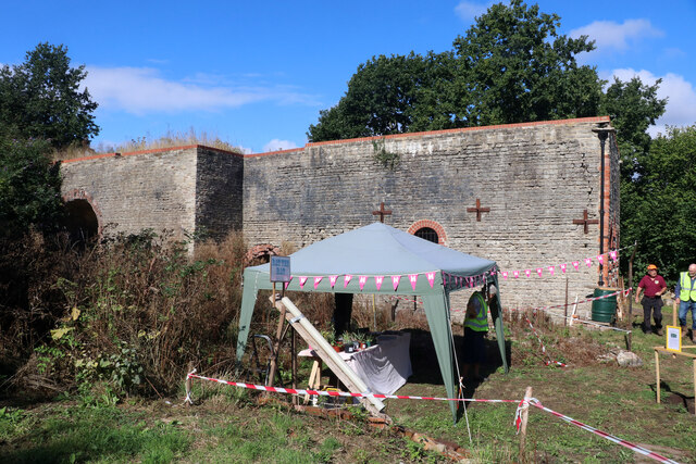 A long stone and brick engine house wall with brick-arched openings, a gazebo and bunting in front of it on an open day.