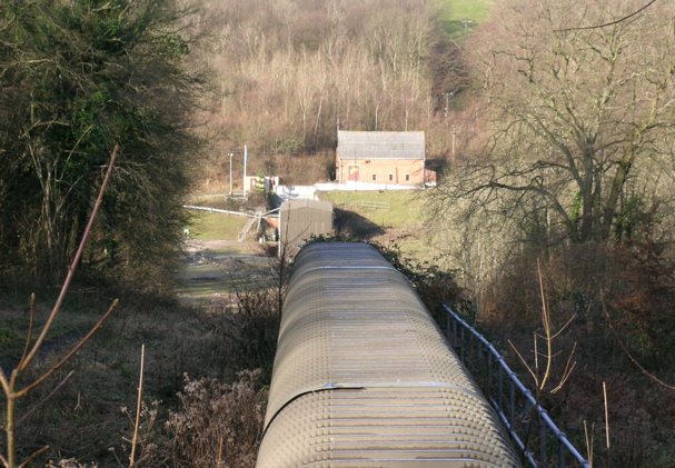 Low industrial buildings and a covered conveyor at the Brightling Mine drift entrance, surrounded by winter woodland.