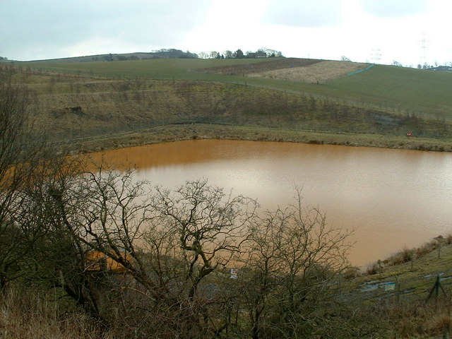 Bright orange ochre staining a shallow watercourse and its banks below a mine water outfall, with rough grass and moorland behind.