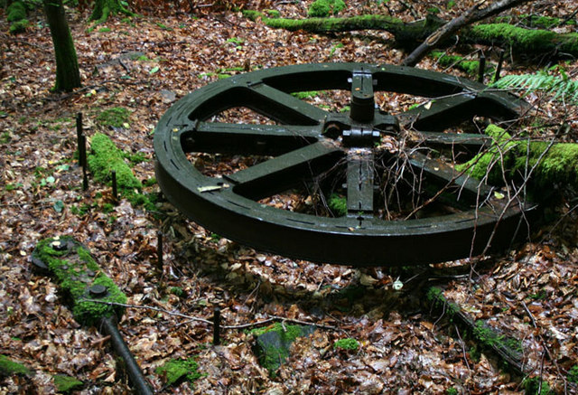 A large rusted iron sheave wheel lying in undergrowth on the hillside, part of the aerial ropeway built in 1917 to carry pyrites across the Conwy valley.