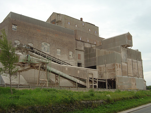 Crushing plant and conveyors at a working limestone quarry, the buildings tinged reddish by the local stone.