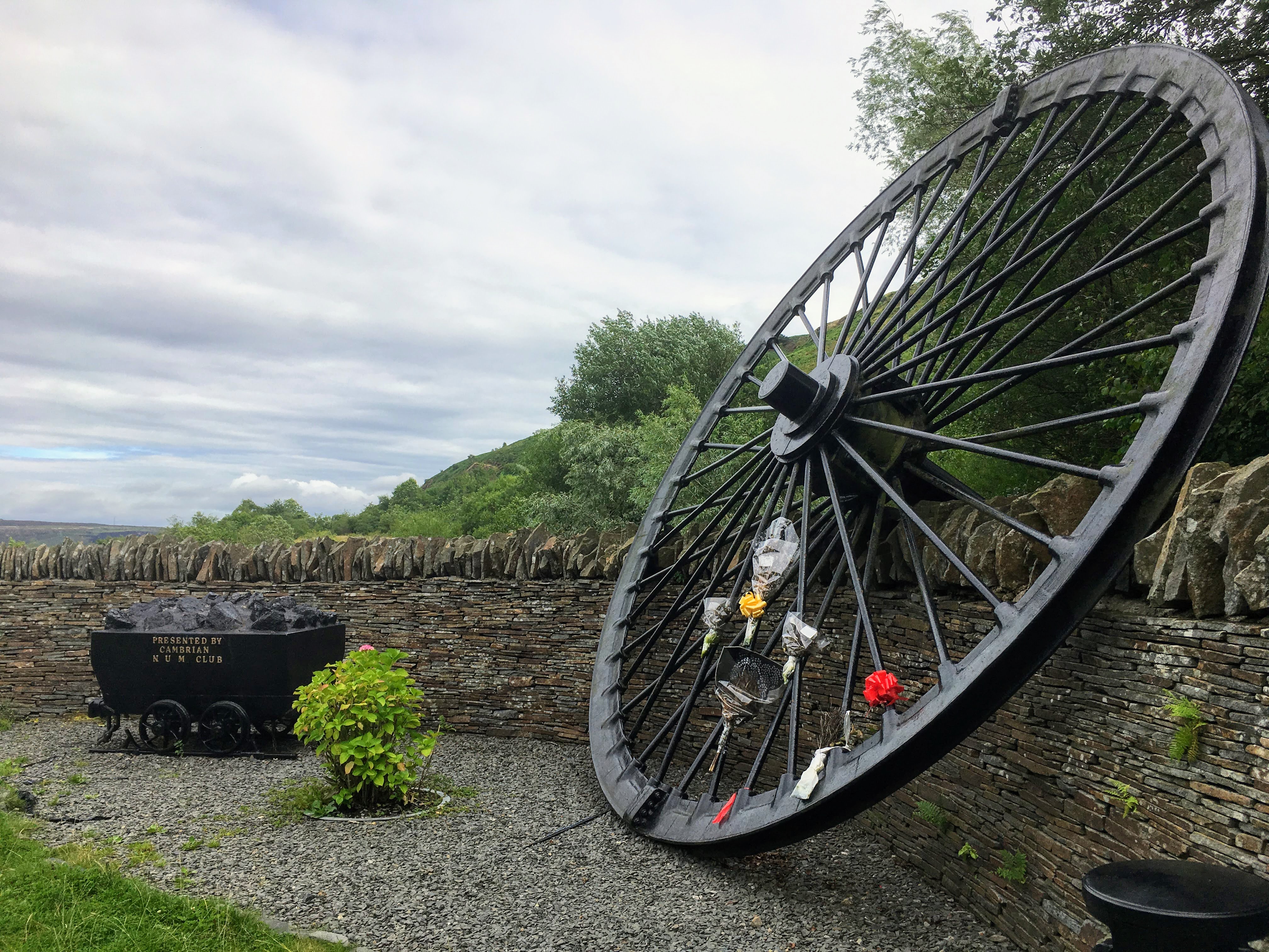 A memorial stone near Clydach Vale commemorating the miners killed in Cambrian Colliery's two explosion disasters, set among grass and low vegetation.