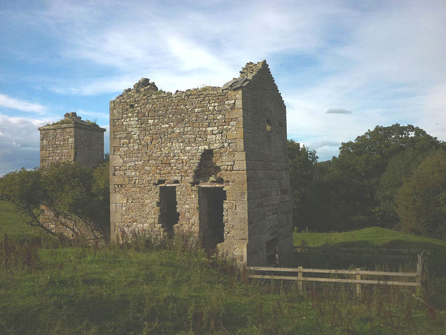 A roofless stone engine house standing to full height in rough pasture, with its detached chimney to the left.