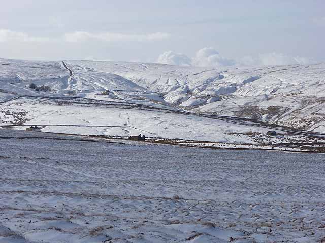 A broad moorland valley head with scattered buildings and pale spoil ground on the far side.
