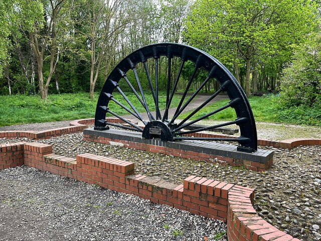 A colliery winding wheel mounted as a monument on grass in Betty Eastwood Park, the public park that now covers the Crigglestone Colliery site