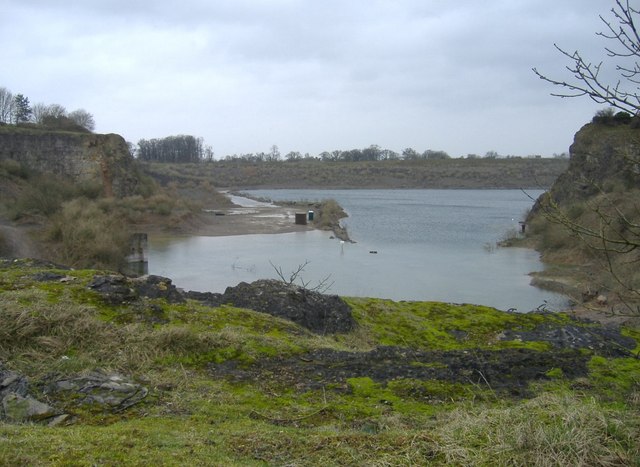 A lake filling a quarry, with grey rock faces at either side and a low shore of bare stone in the foreground.