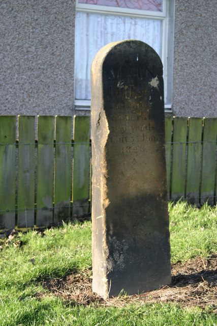 A low inscribed stone beside a suburban footpath, the marker recording the distance from the colliery pit to the Main Dyke.