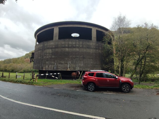 The round, windowed concrete tower of the former Hafodyrynys coal washery beside a roadside lay-by, with a horse in the field behind.