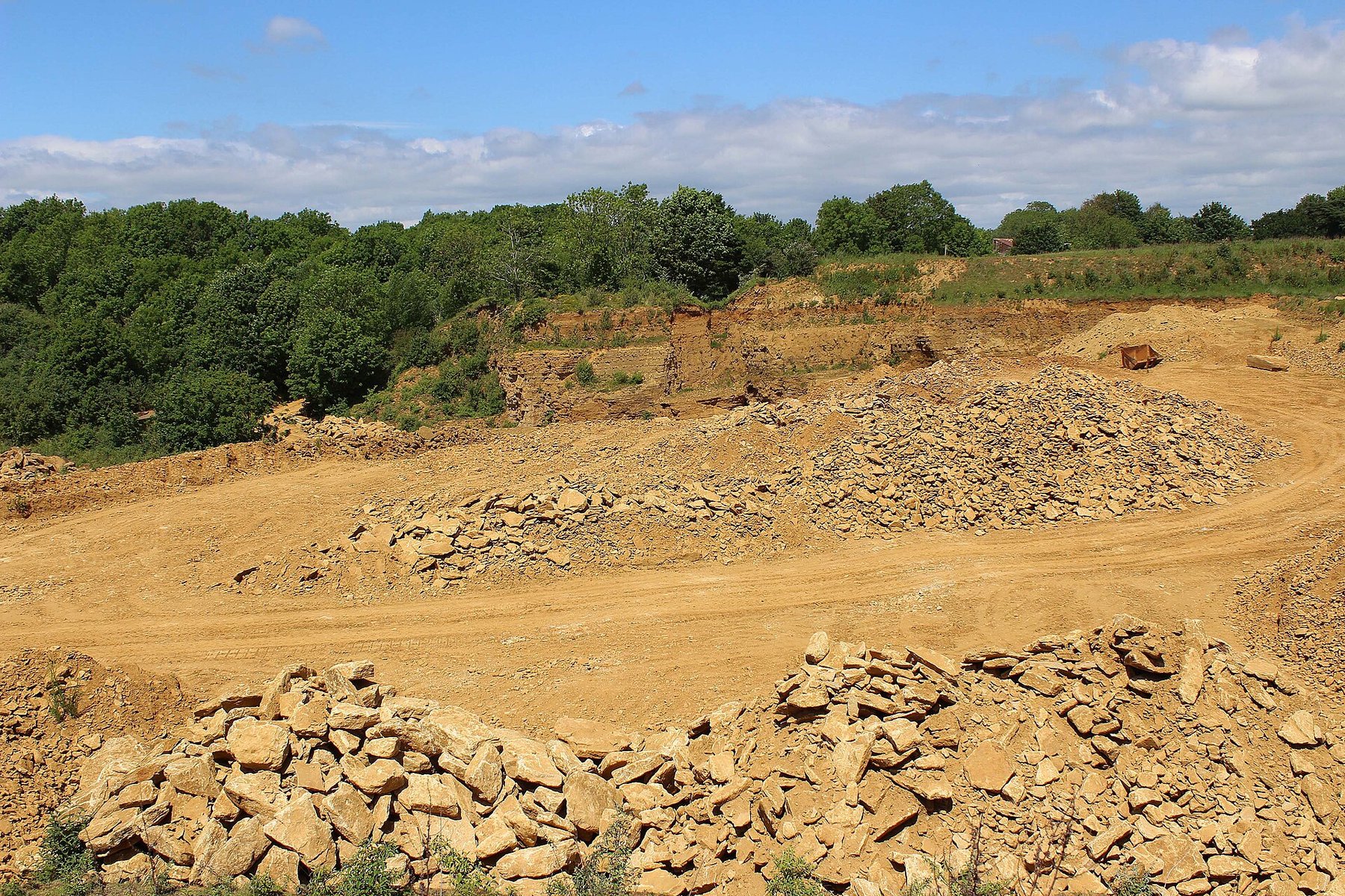 A working face of honey-coloured hamstone on Ham Hill, Somerset, showing the bedded Jurassic limestone and cut blocks in the quarry below