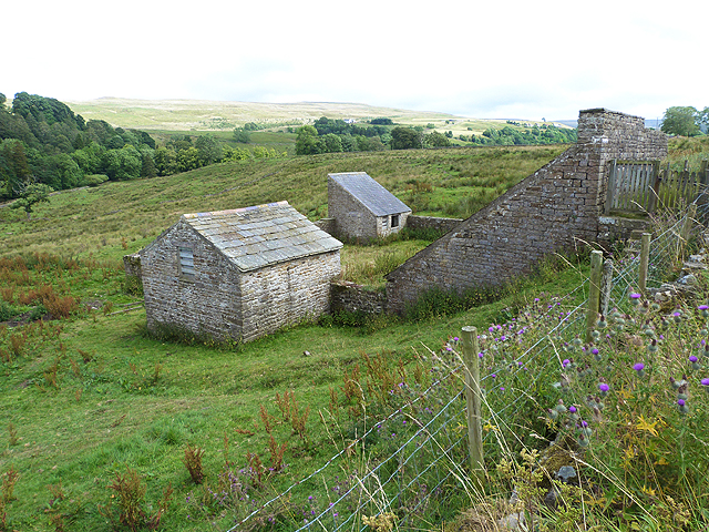 Two small stone buildings with slate roofs beside a high stone wall enclosing the ore-storage bays, on rough grassland above the valley.