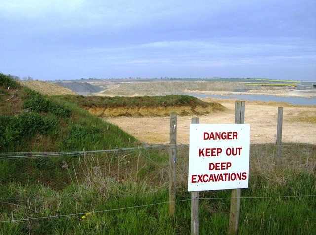 A wide worked-out limestone quarry with grassed benches and a pale rock face, looking north from the footpath at the north-western end.