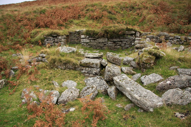 Low ruined granite walls and fallen blocks on a grassy hillside with brown bracken.