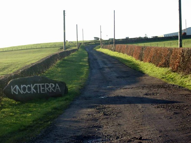 The road end of Knockterra farm on the Skares road near Cumnock, with a farm track leading off between fields under a grey sky