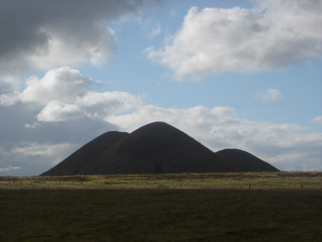A grassed-over conical coal bing standing above rough open ground on the moorland edge at Fauldhouse, West Lothian.