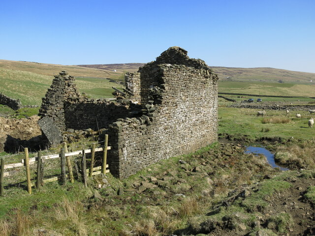 A roofless drystone building standing gable-high on open moorland, with walled pasture and fells beyond.