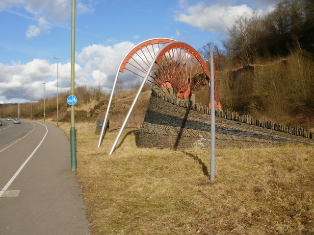 A memorial in the former colliery village depicting colliery winding wheels, dedicated to the Oakdale miners, standing beside a stone plaque on the B4251.