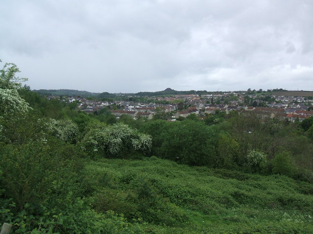 A steep conical colliery spoil tip with a bare grey surface rising above the rooftops of Midsomer Norton, with the town and fields beyond.