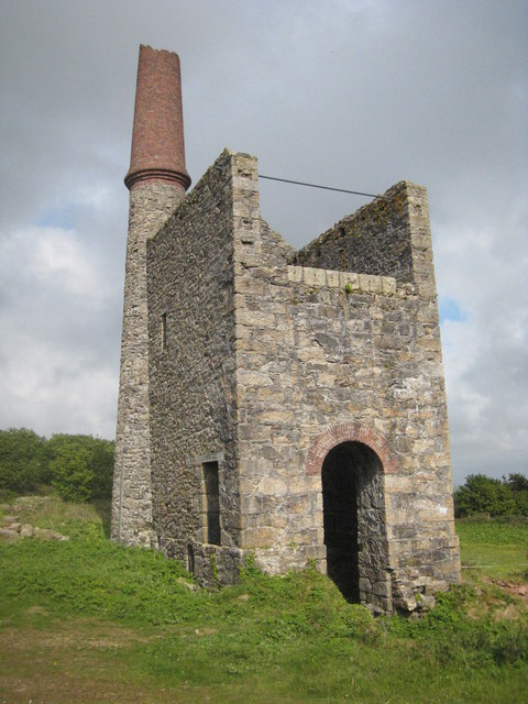 A roofless stone engine house with an arched doorway and a tall chimney topped with red brick.
