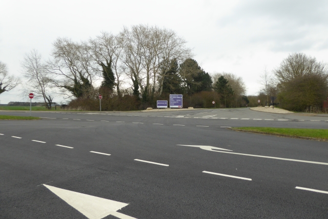 A wide empty road junction with fresh markings leading to a business park sign among bare trees, on the cleared site of the colliery.