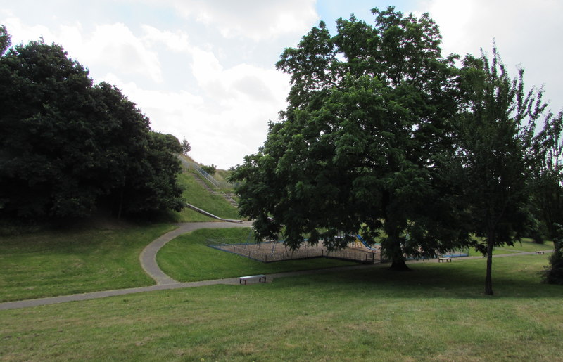Mown grass and scattered trees laid out as a public park within the floor of the former Rumney quarry, its old rock faces rising behind