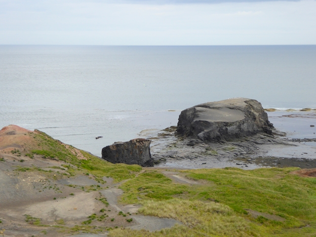 A bare, reddish headland of quarried shale running out to the sea, with the rocky nab and a detached stack beyond.