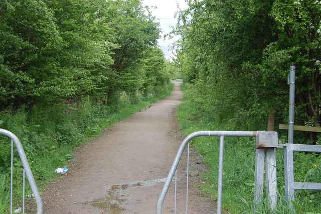 A muddy tree-lined lane running away between hedges, with metal barrier rails at the entrance in the foreground, 2009