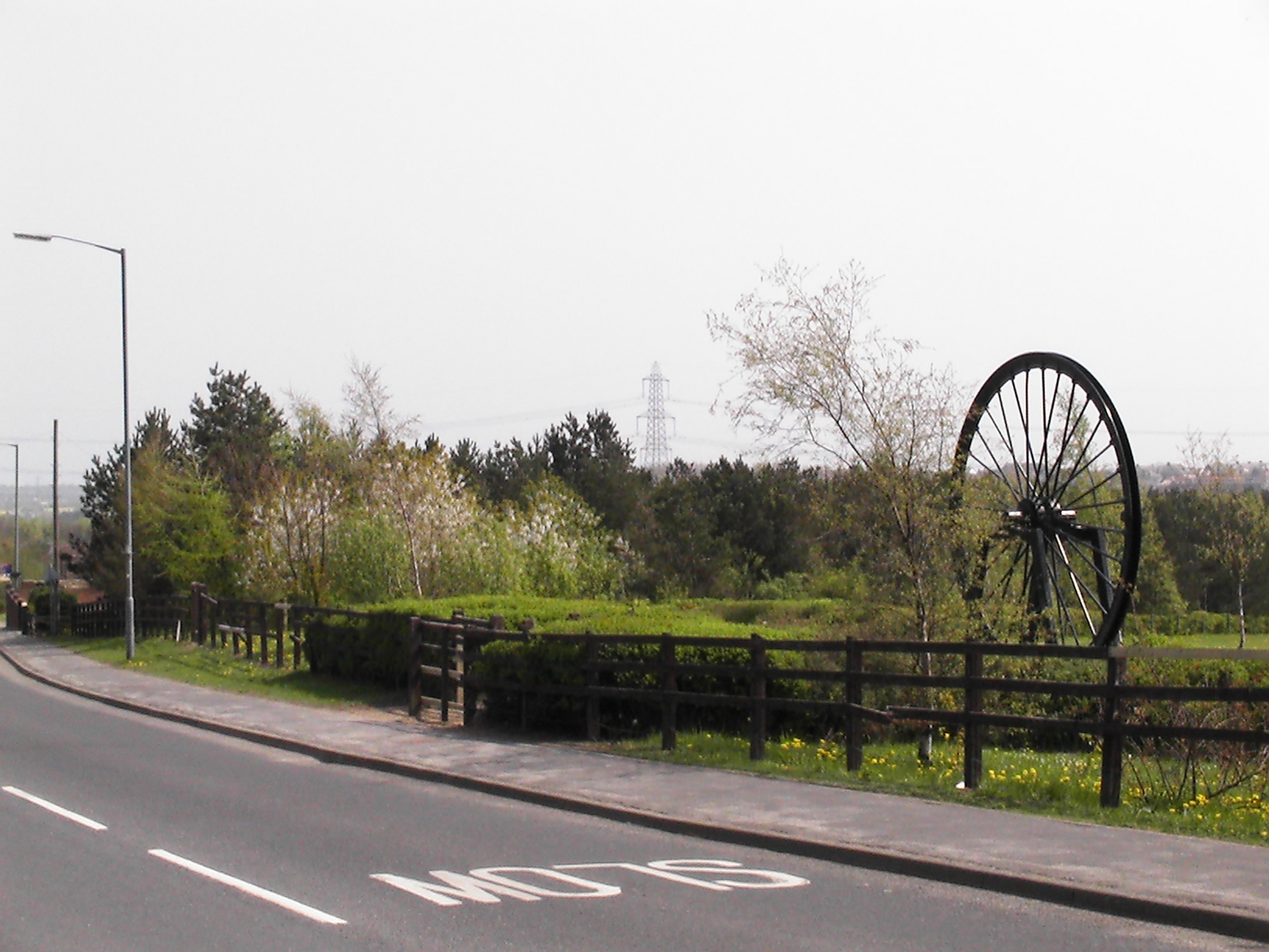 A colliery pit wheel mounted as a memorial at the site of the former Thornley Colliery, County Durham, with woodland behind marking where the colliery once stood