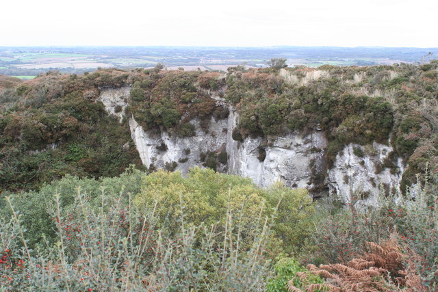 A deep hollow with pale white clay walls, its rim overgrown with heather and scrub, and farmland stretching to the horizon beyond.