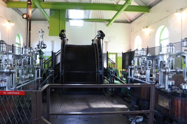 A large horizontal twin-cylinder steam winding engine with its rope drum, standing in a whitewashed engine house behind a railing.