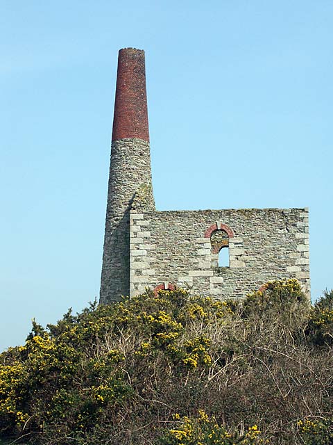 The surviving three-storey engine house at Batter's Shaft, West Chiverton Mine, seen from the adjacent field; a stone chimney rises from the centre of the building's rear wall.