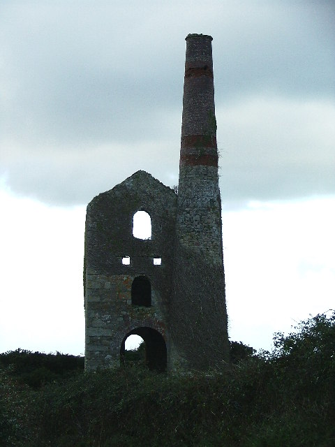 A stone-built, roofless Cornish engine house with an attached chimney stack, standing alone in open farmland near St Day.