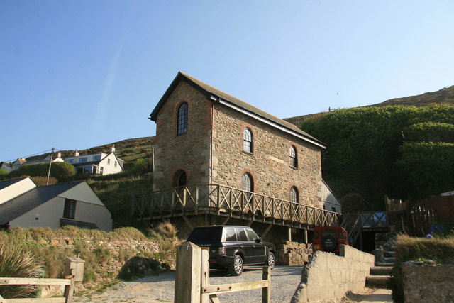 A tall two-storey stone engine house with arched windows, now a home, beside a lane at Porthtowan.