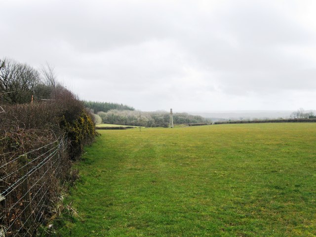 A lone stone mine chimney stands at the far side of a grassy field bordered by a hedge.