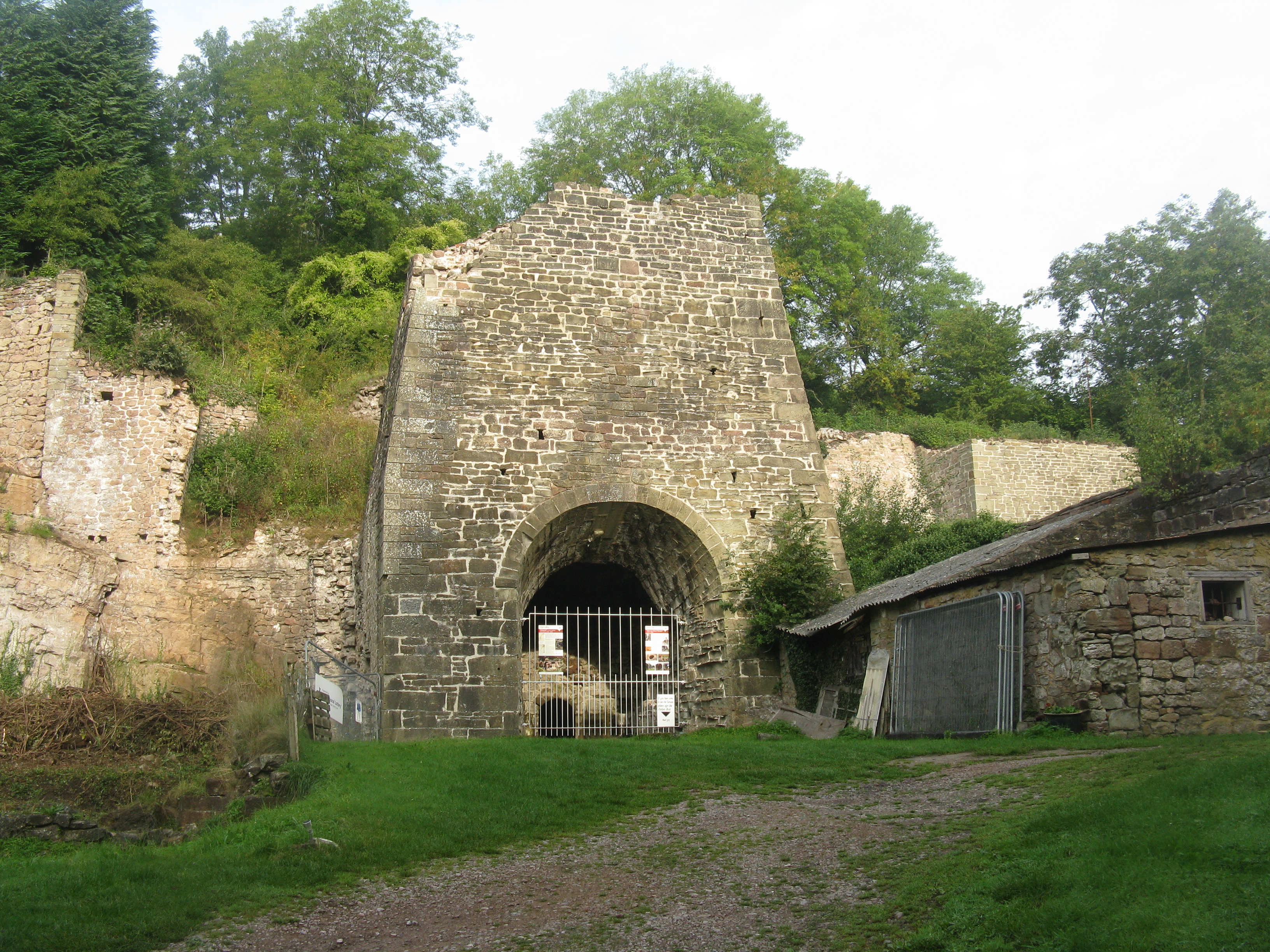 The surviving stone-built 1806 blast furnace structure at Whitecliff Ironworks, Coleford, set against its limestone cliff