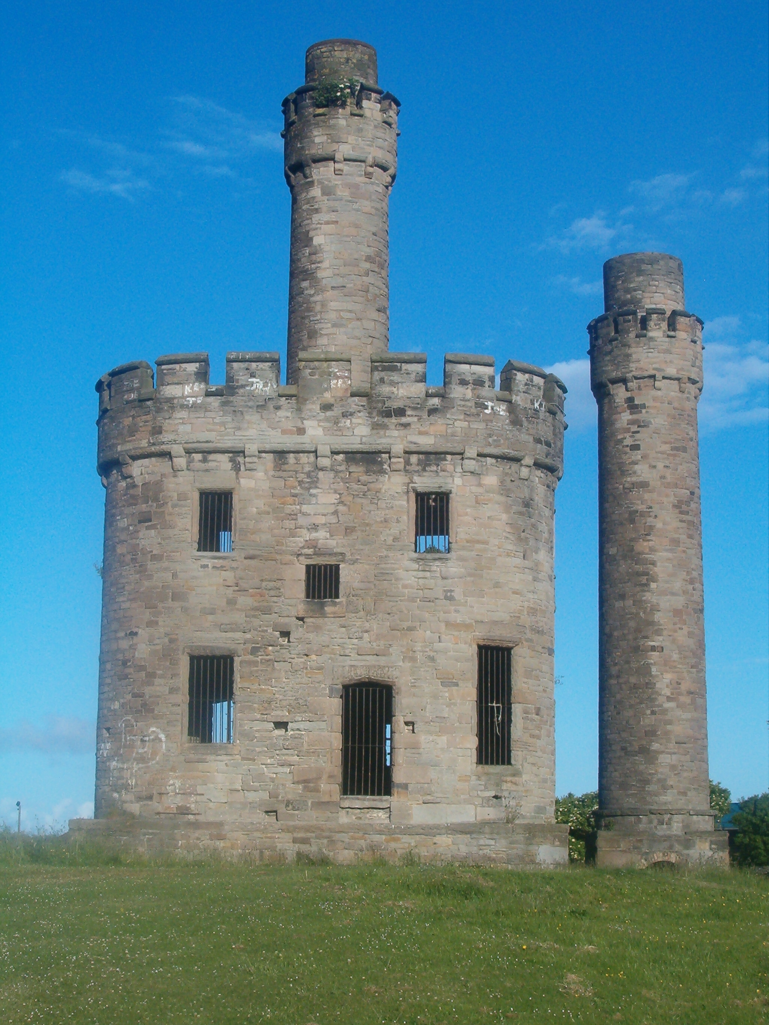 The preserved ruins of Jane Pit at Workington: a castellated stone engine house and tapering chimney standing in open grass.