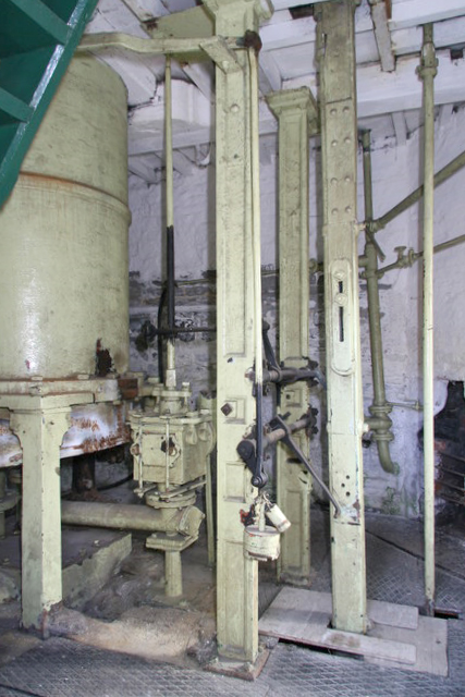 The pale-painted cylinder, valve gear and iron columns of a beam pumping engine inside its whitewashed engine house.