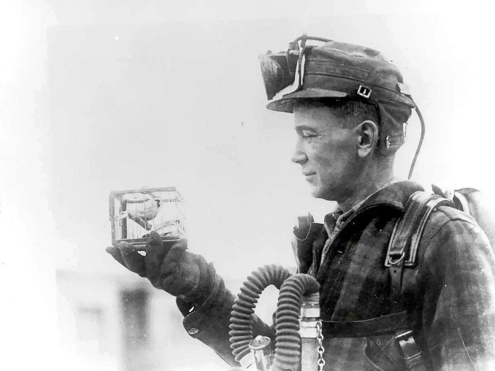 A mining foreman displaying a small cage containing a canary, used to detect carbon monoxide gas in coal mines, 1928.