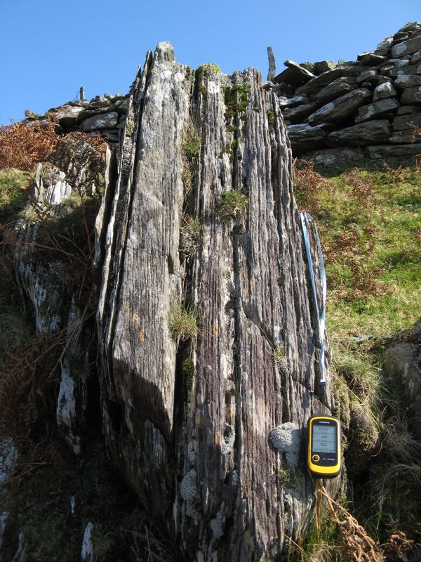 A slate face showing closely spaced parallel cleavage planes cutting across the rock, with joints running at an angle to them.