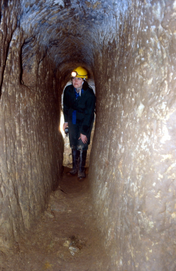 A narrow, hand-dug mine passage with a coffin-shaped cross-section, wider at shoulder height and narrowing above and below