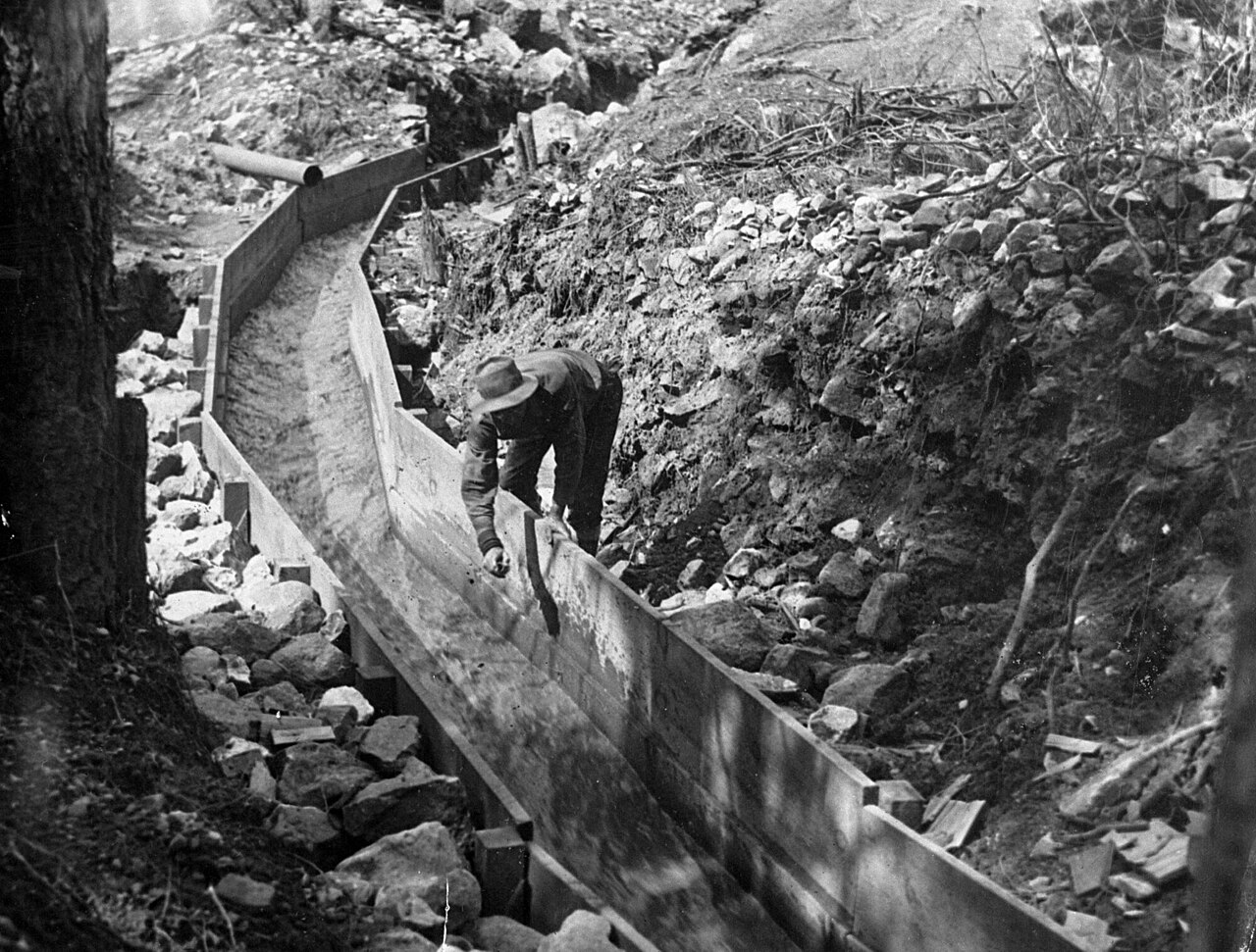 A miner working a wooden sluice box, California, between 1890 and 1915 — the same gravity-and-water extraction principle used for alluvial gold panning in Britain.