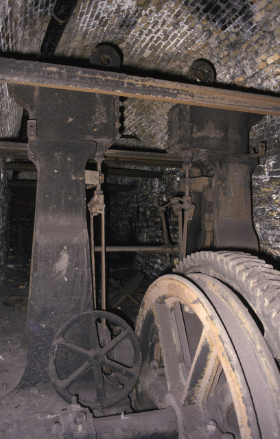 A stationary steam haulage engine with its drum and gearing, standing in a ruined engine house.