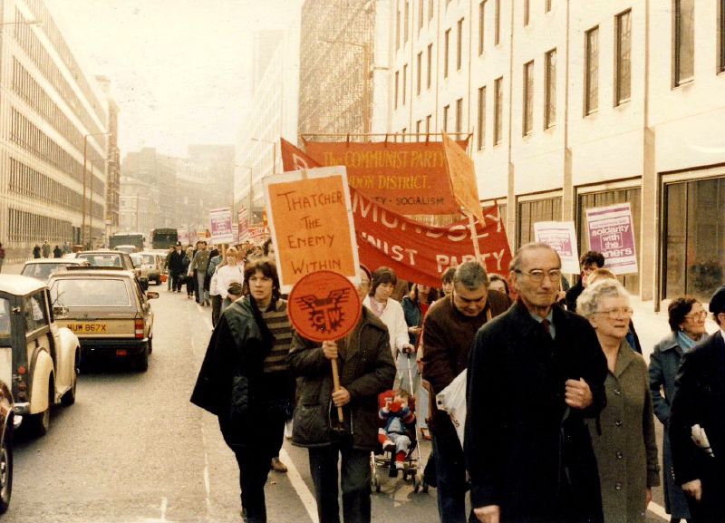 A large crowd of demonstrators marching through London in 1984 in support of striking miners, carrying union and campaign banners.