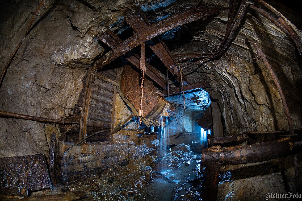 A timber-framed ore pass and chute scoop inside an abandoned underground lead mine, showing the sloped channel and its supporting timberwork.