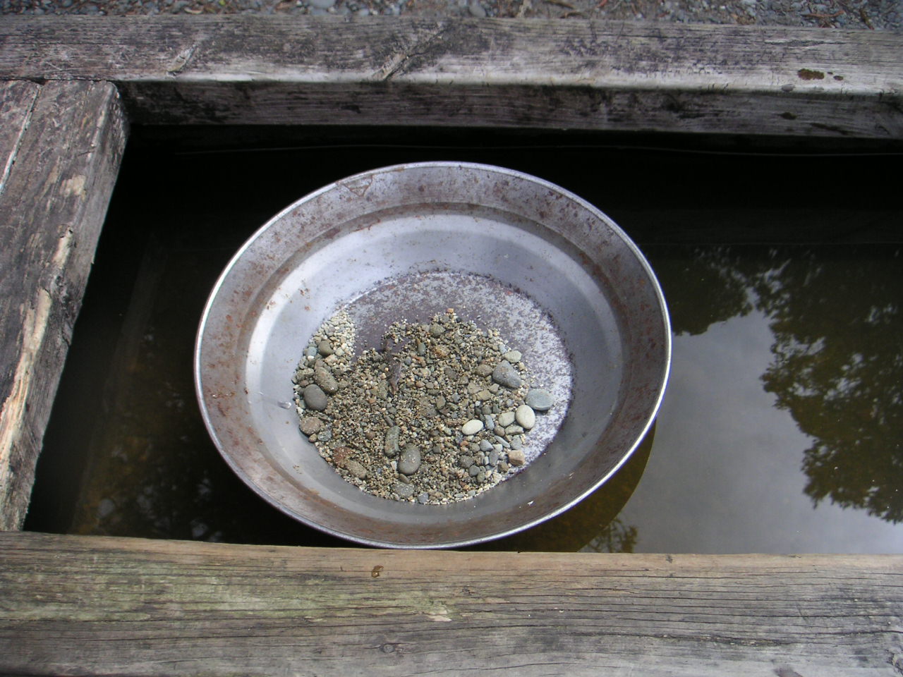 A metal gold pan with sloped sides and riffled edges, the basic tool of panning.