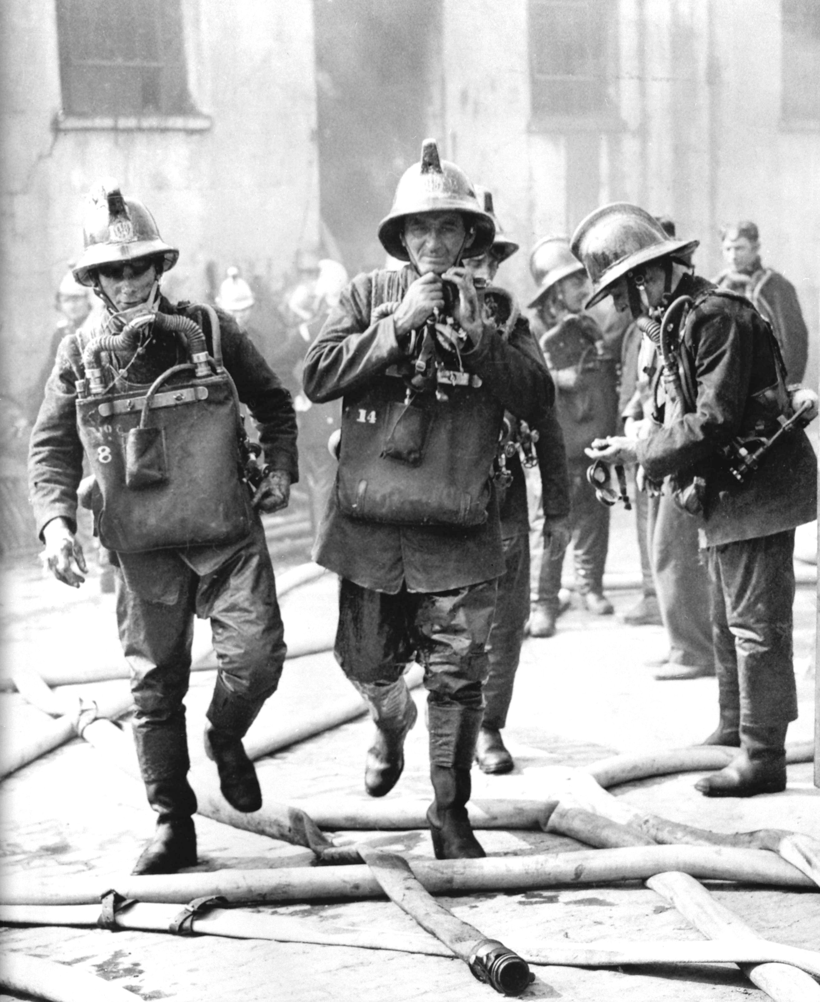 Two firemen wearing Siebe Gorman Proto Mark IV oxygen breathing apparatus, the same design used by British mines rescue teams for most of the 20th century.