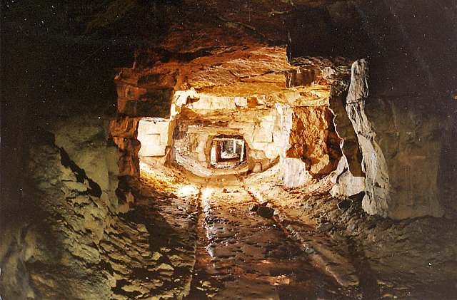 An underground gallery at Firs Quarry, part of the Combe Down Bath stone mines, showing worked rock walls and an old tramway track running between the room-and-pillar workings.