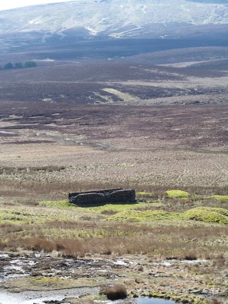 The low stone walls of a rectangular wheelpit standing on open moorland, with the fell rising beyond.